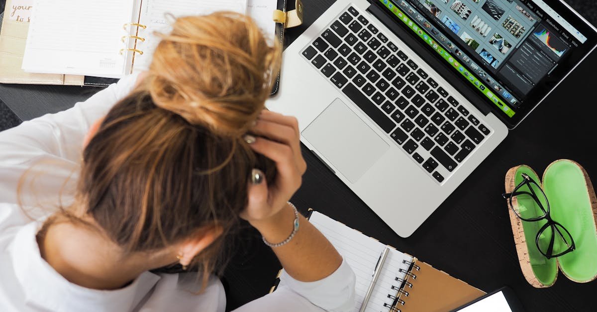 Overhead view of a stressed woman working at a desk with a laptop, phone, and notebooks.