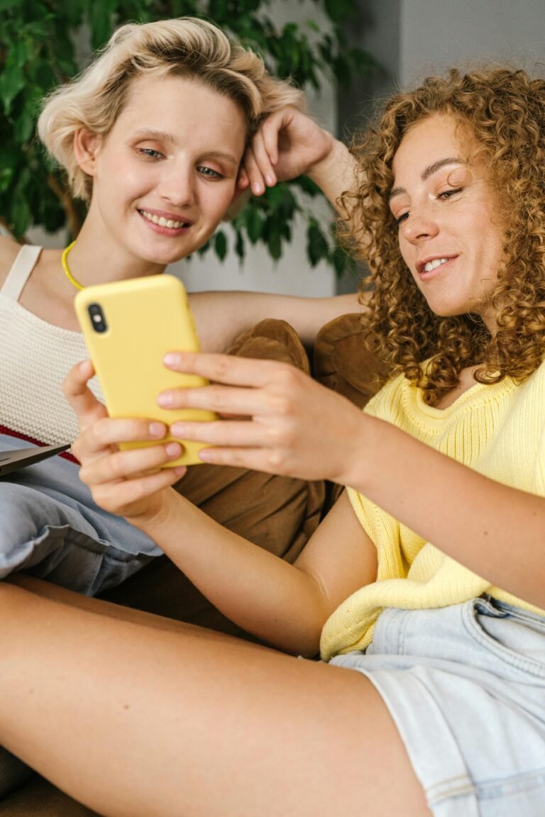 Two friends enjoying time together indoors while looking at a smartphone.